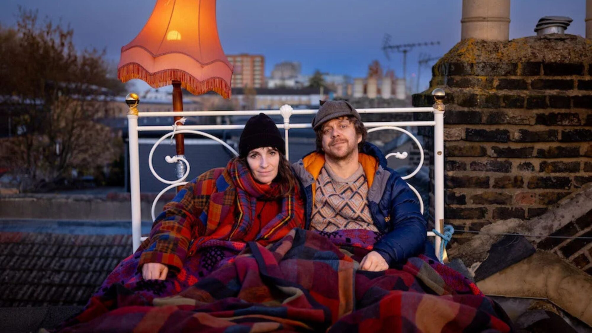 Couple sat on a rooftop in bed with a lamp